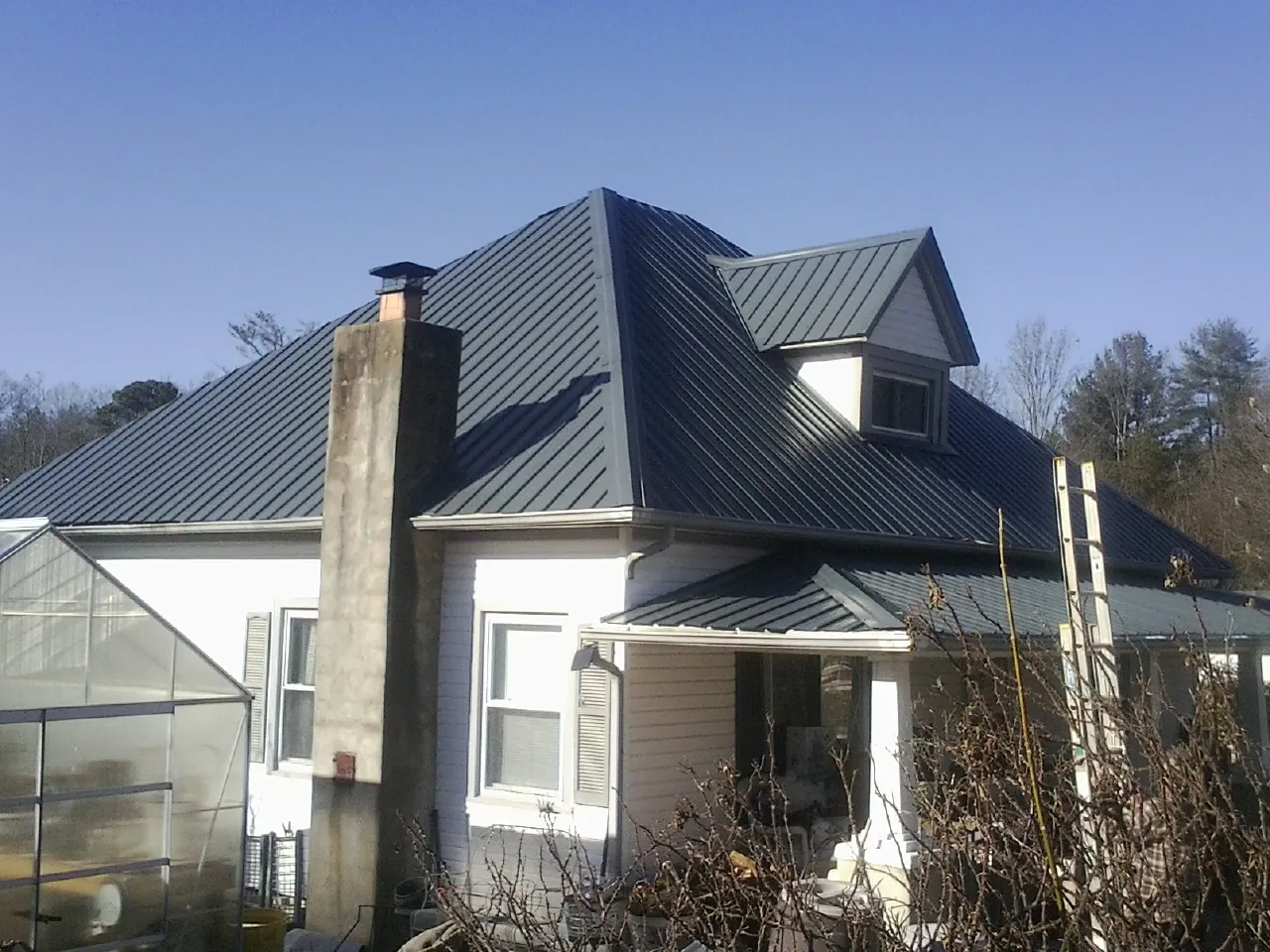 Dark blue standing seam metal roof on a white farmhouse with dormer — Slate & Tile Roof Repair by Roofing Brothers in Glenside