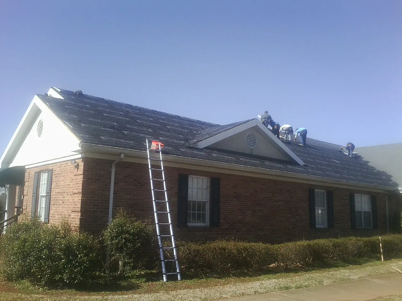 Crew tearing shingles off a brick ranch roof with a ladder set — Emergency Roof Repair work by our crew in Glenside