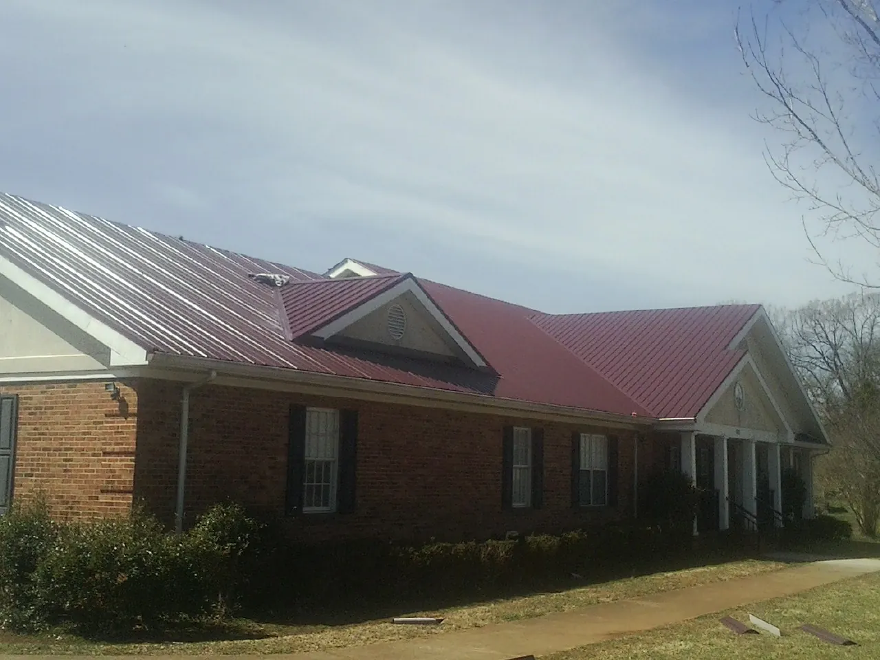 Red metal roof with gabled entries on a long brick building, from a Hail Damage Roof Repair job in Glenside