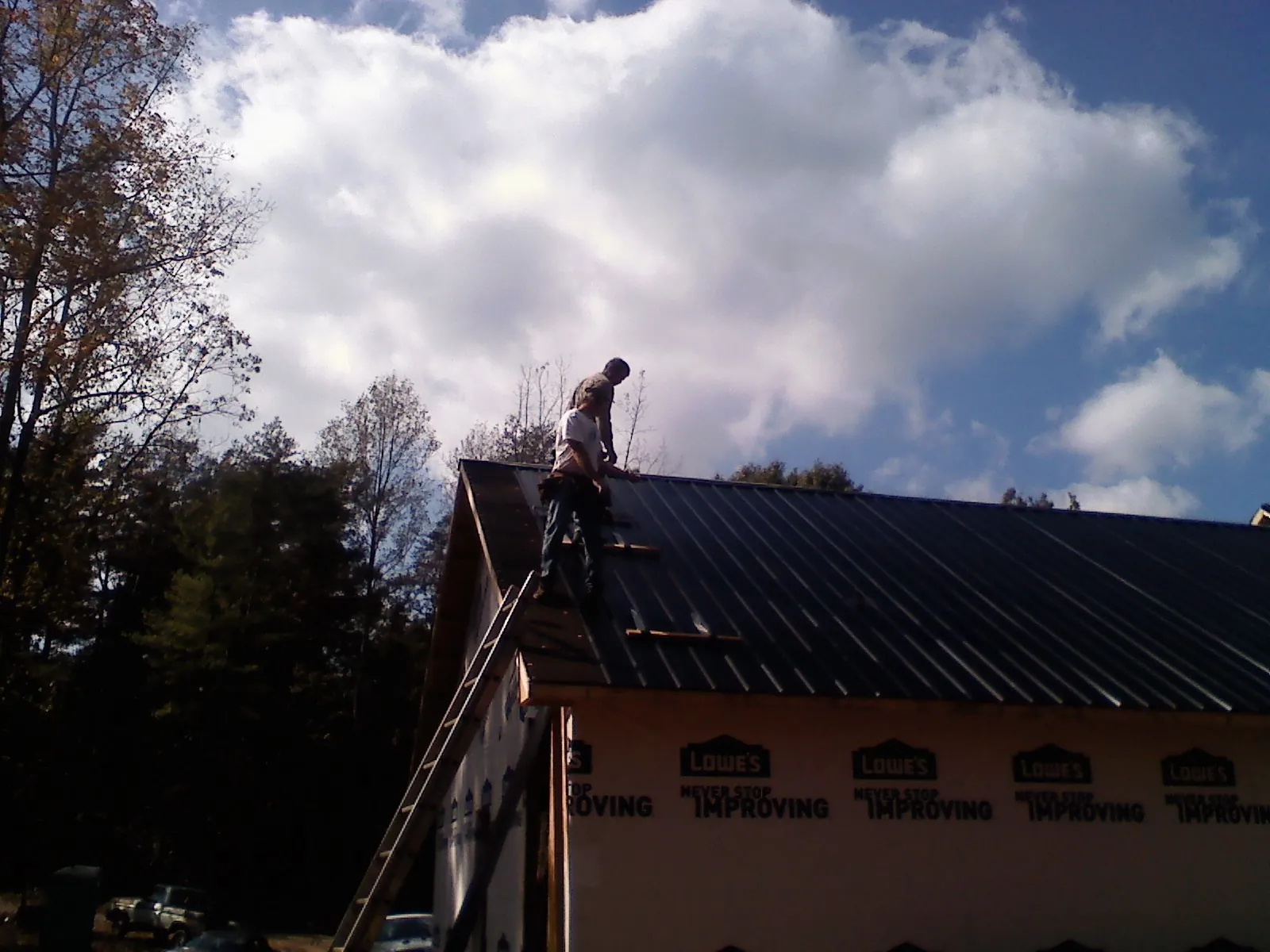 Roofer fastening dark metal panels high against a cloudy sky, from a Roof Inspection job in Glenside