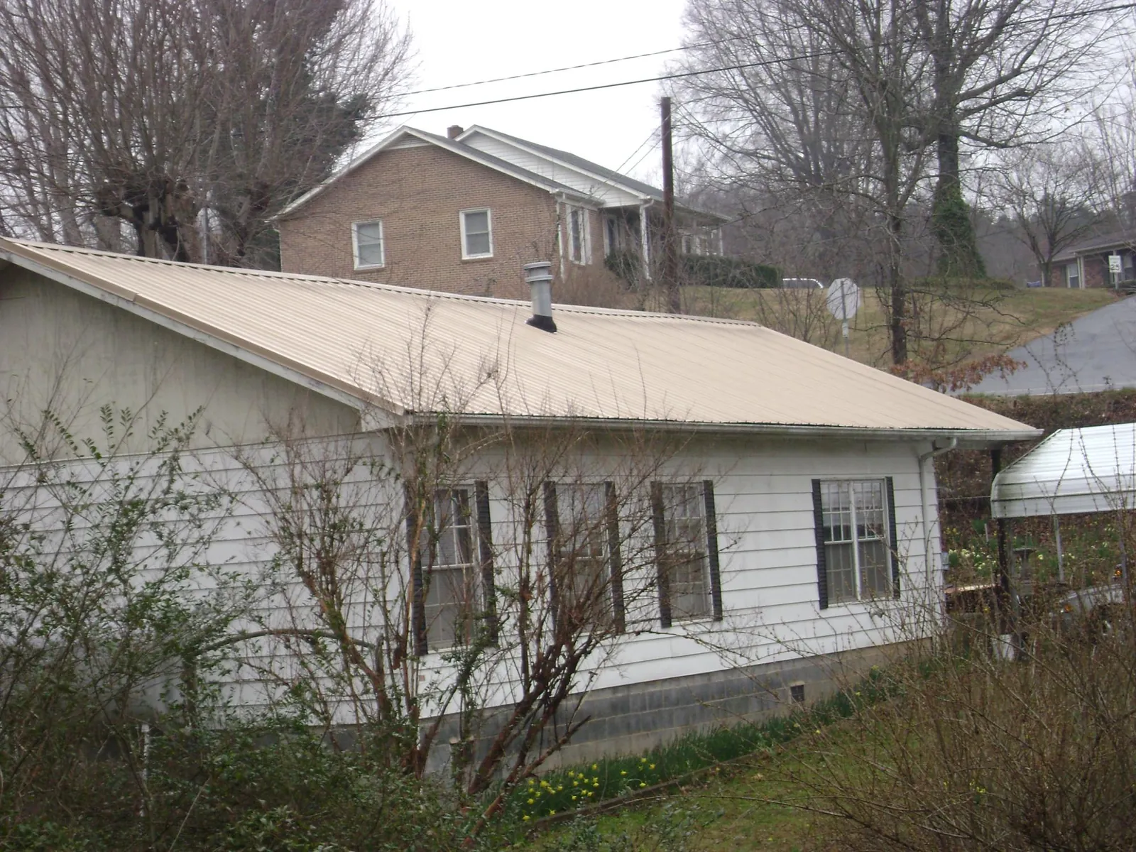 Tan metal roof on a white sided house set into a hillside — Commercial Roofing by Roofing Brothers in Glenside